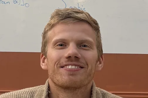 Gui smiling at a desk in front of a whiteboard of math.